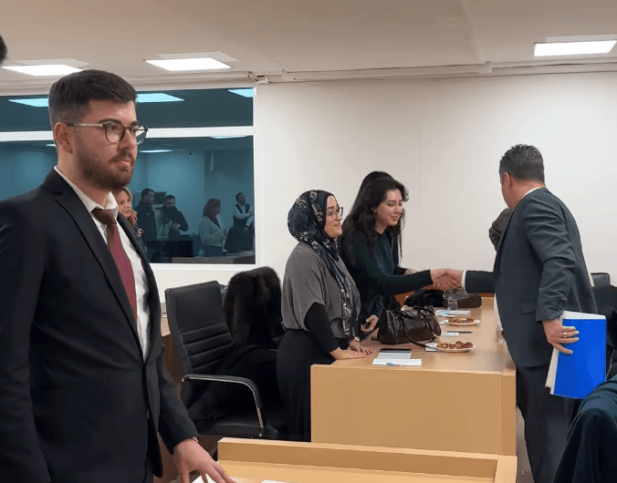 Çorlu Belediyesi Gençlik Meclisi toplantı salonunda, belediye yetkilisi üyelerle tek tek tanışırken; ön planda genç bir erkek üye görülüyor.