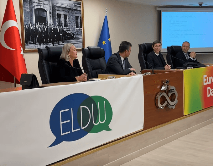 Çorlu Belediyesi Gençlik Meclisi toplantısını yöneten divan heyeti masası; arkada Atatürk portresi ve Türk bayrağı, önde ise Avrupa Yerel Demokrasi Haftası (ELDW) logolu pankart yer alıyor.