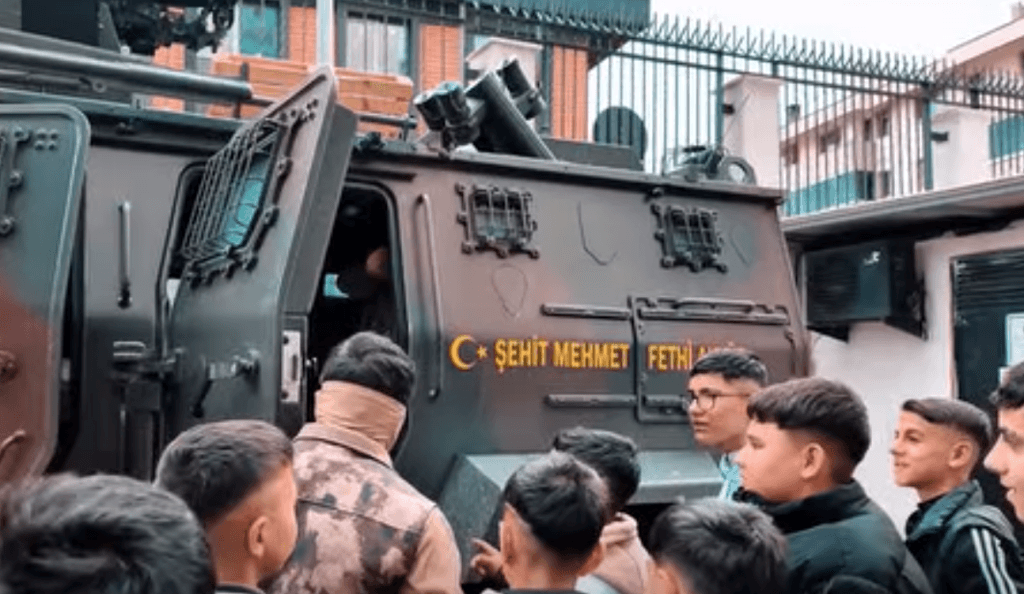 Emniyet Müdürlüğü bahçesinde sergilenen "Şehit Mehmet Fethi Akyüz" isimli zırhlı polis aracının etrafında toplanan öğrenciler, aracı merakla inceliyor.