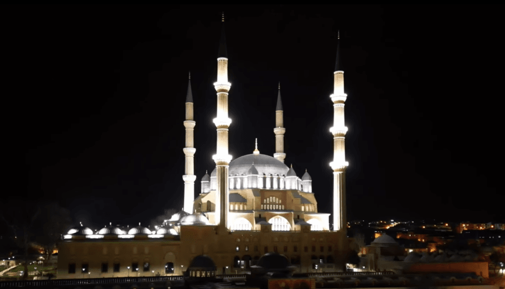 Edirne şehrinin üzerinde parlayan bir mühür gibi duran Selimiye Camii'nin kuş bakışı gece görüntüsü; aydınlatılmış ana kubbe ve göğe uzanan dört minare.