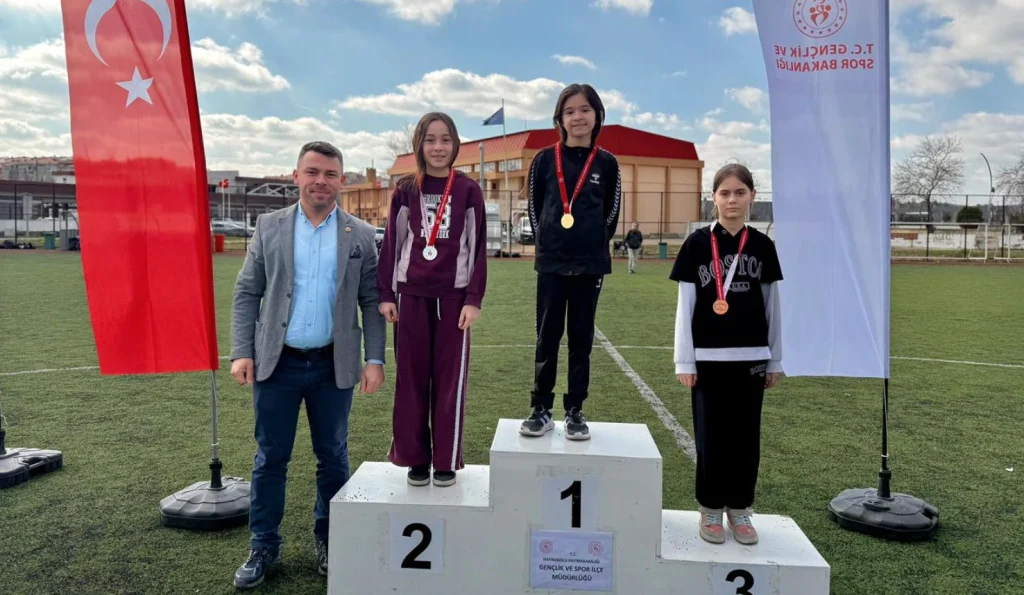 Atletizm yarışmasında dereceye giren kız sporcular kürsüde madalyalarıyla.