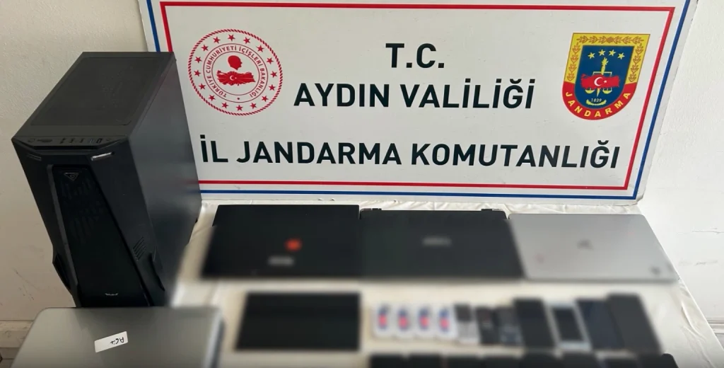 Aydın İl Jandarma Komutanlığı tarafından düzenlenen operasyonda ele geçirilen masaüstü bilgisayar, laptoplar ve çok sayıda dijital materyal sergileniyor.