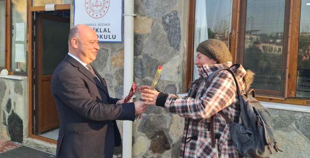 Bozcaada Belediye Başkanı Yahya Göztepe, İstiklal Ortaokulu önünde bir kadın çalışana 8 Mart Dünya Emekçi Kadınlar Günü vesilesiyle çiçek takdim ederken.