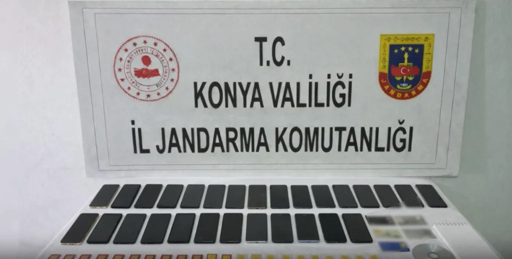 Konya İl Jandarma Komutanlığı masasında sergilenen, vatandaşları dolandırmak için kullanılan onlarca akıllı telefon ve sim kart düzeneği.