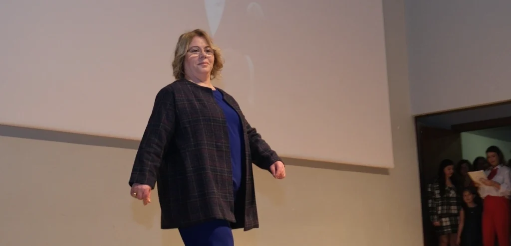 Uzunköprü Belediyesi Üreten Kadınlar Moda Gösterimi'nde, el yapımı şık bir ceketle podyumda yürüyen kadın katılımcı.