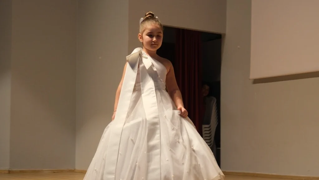 Uzunköprü Belediyesi moda gösterimi kapsamında el emeği beyaz tasarım kıyafetiyle podyumda yürüyen küçük model.